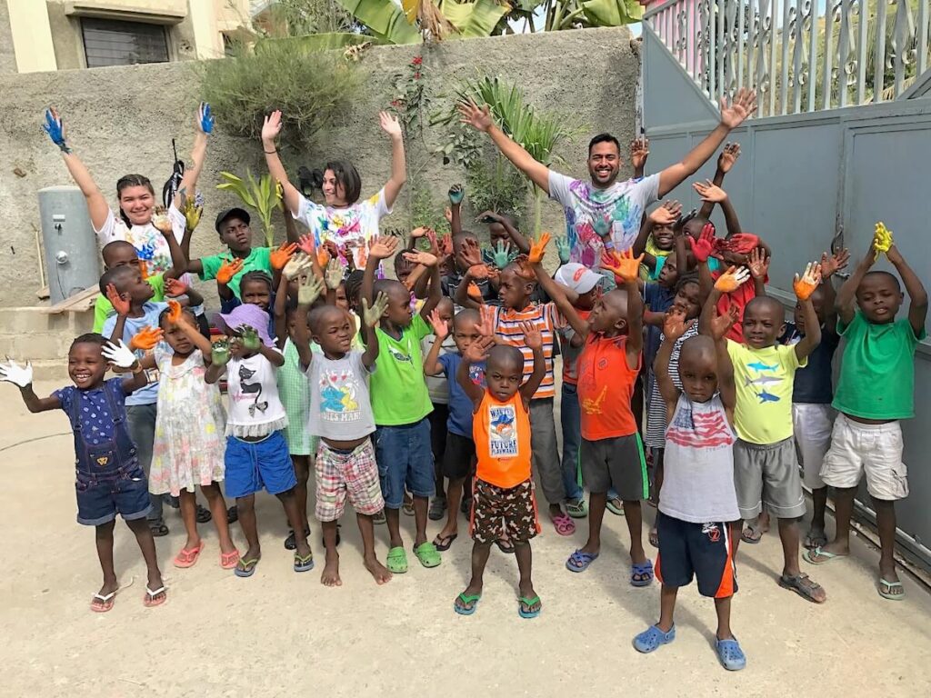 A group of happy kids and volunteering adults with their hands covered in paint from an activity 