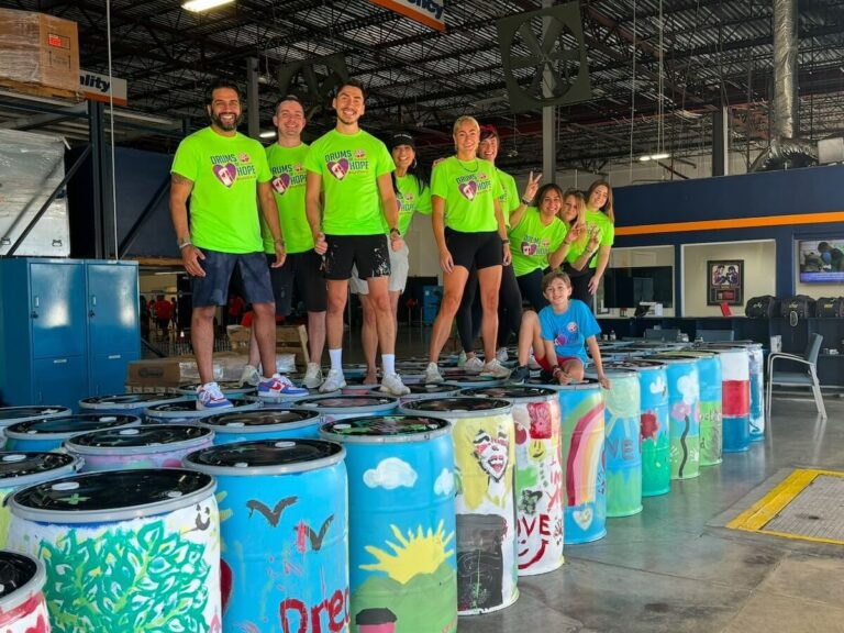 Volunteers standing on dozens of drums of food being sent to food insecure countries by It's 4 the Kids